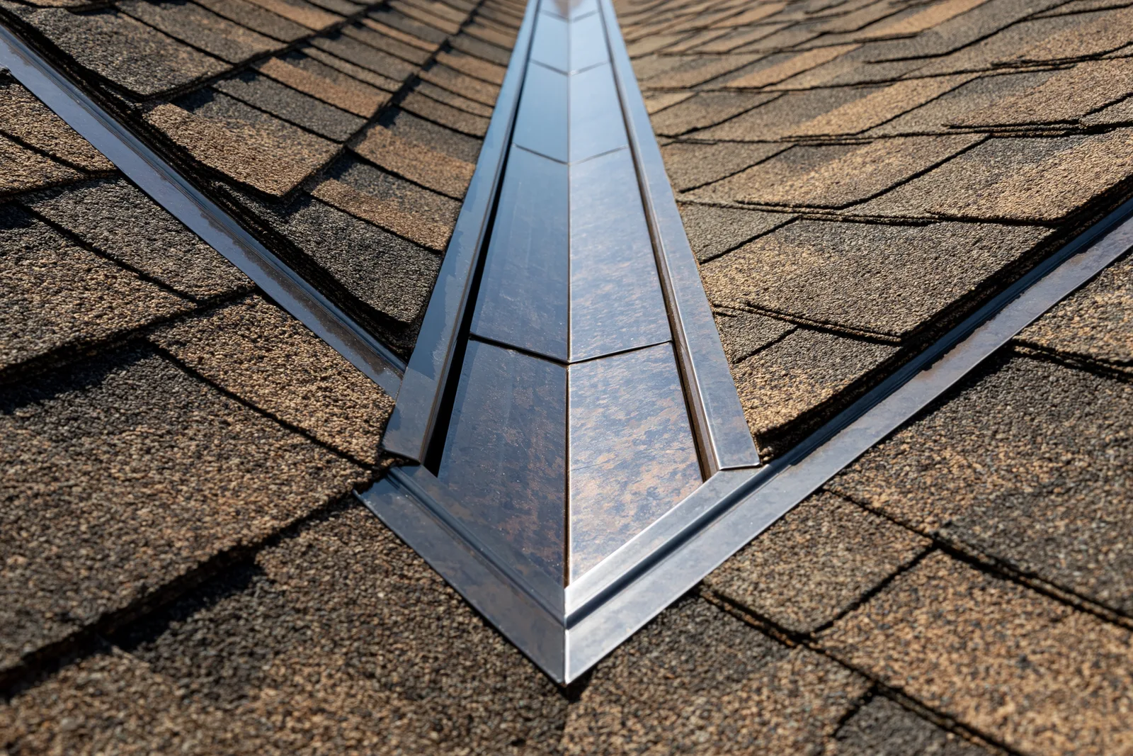 Metal valley flashing running down a tan shingle roof at a hip intersection