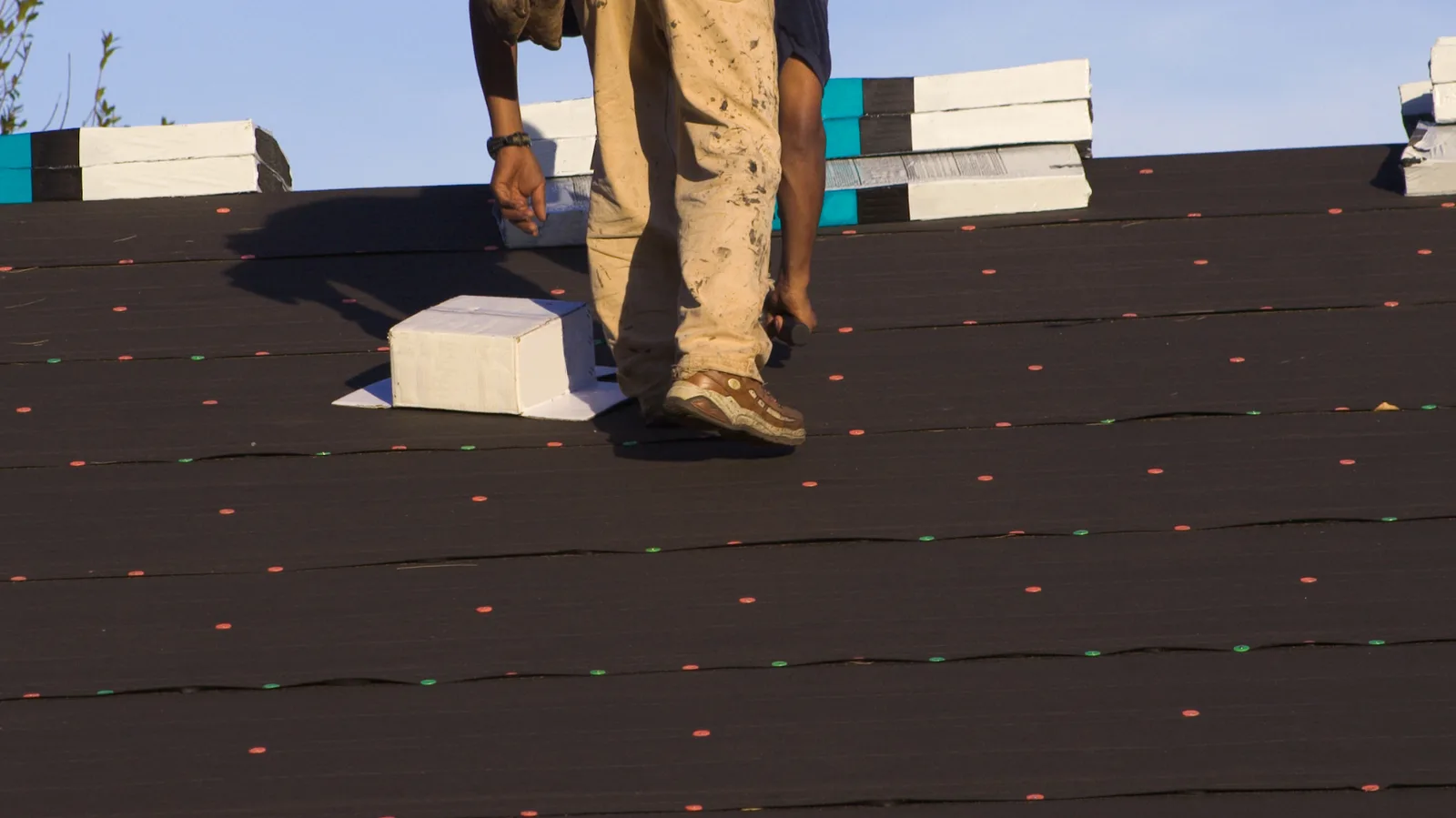 A roofer walking across underlayment near stacked shingle bundles