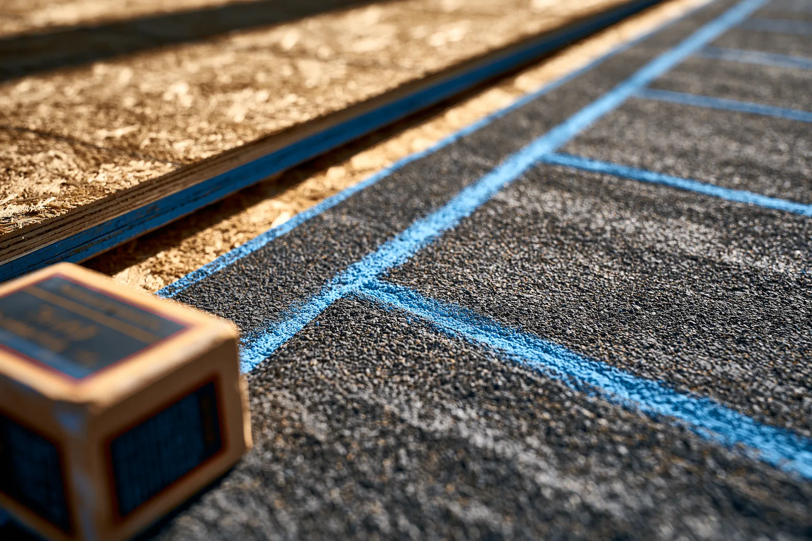 A blue chalk line snapped across underlayment beside exposed roof decking
