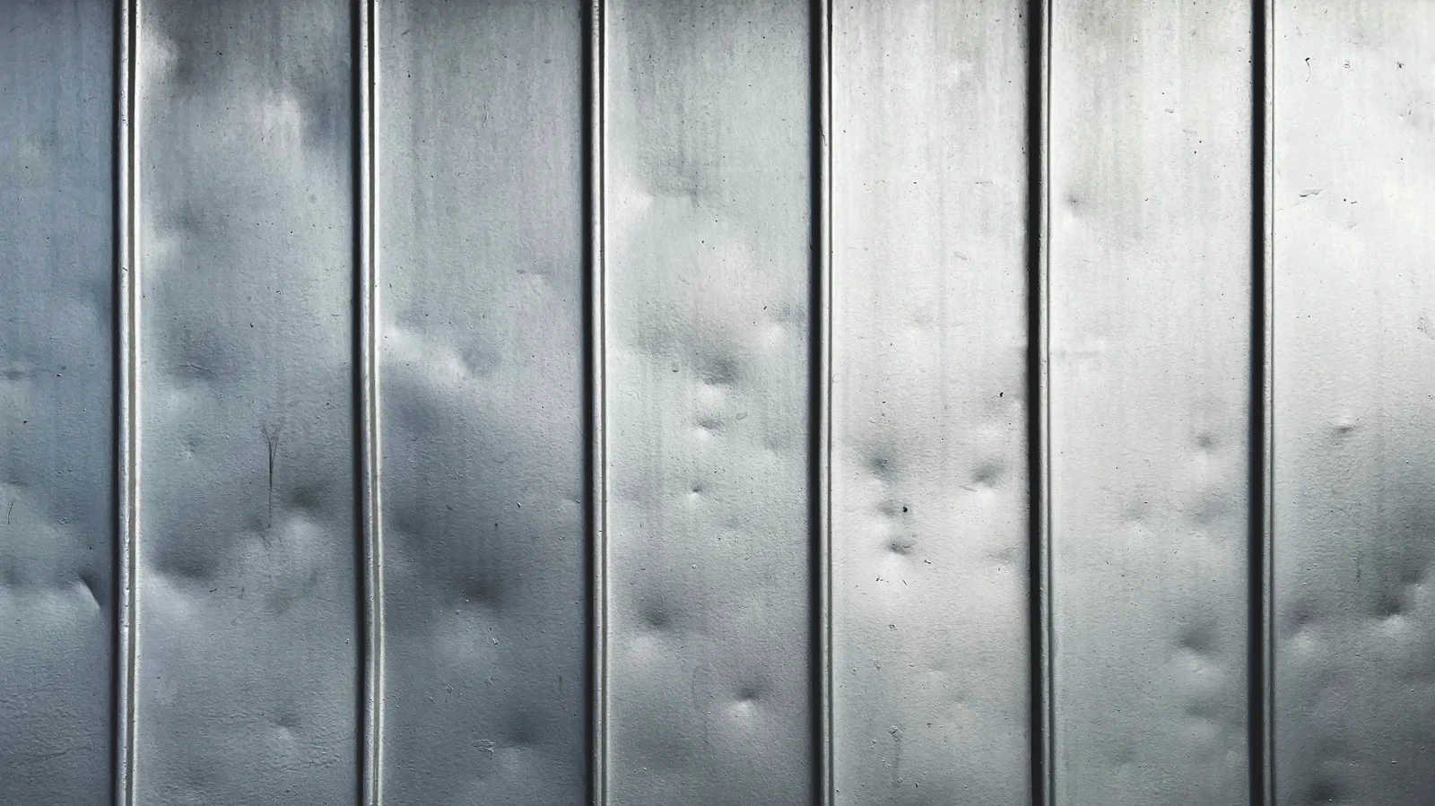Small dents scattered across ribbed sheet metal panels